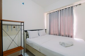 Un lit bien fait, avec une couette blanche et deux oreillers, une étagère en bois et une fenêtre avec des rideaux.