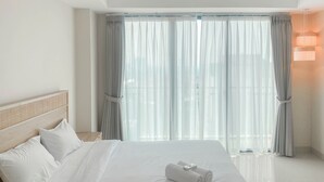 Ein Hotelzimmer mit einem großen Bett, weißen Leinentüchern, einem Holzkopfende und transparenten Vorhängen.