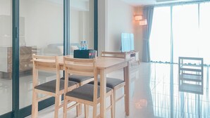 Ein modernes Hotelzimmer mit einem Holztisch, Stühlen, einem kleinen Tisch mit Wasserflasche und einem großen Fenster mit Vorhängen.
