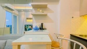 Una cocina moderna con encimera blanca, un hervidor y una cafetera. Hay una zona de comedor con una mesa y sillas.