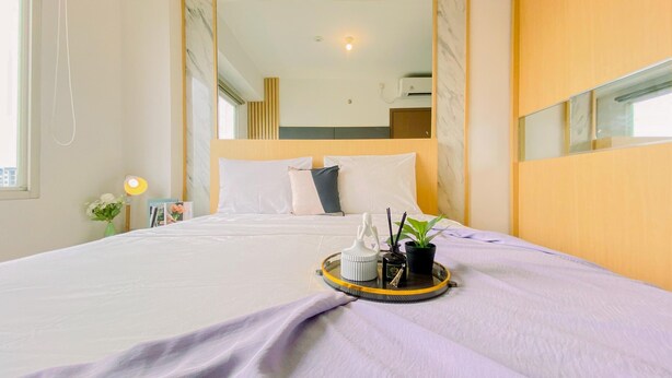 A neatly made bed with a tray of toiletries, a bedside lamp, and a small plant. - Good Place 2BR at Podomoro Golf View Apartment (Gunung Putri)