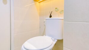 A modern bathroom with a white toilet, tiled walls, and a yellow accent light. - Good Place 2BR at Podomoro Golf View Apartment (Gunung Putri)