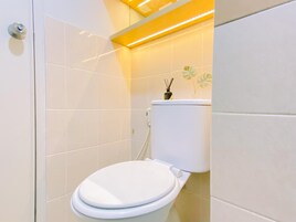 Une salle de bain moderne avec des toilettes blanches, des murs carrelés et un éclairage d’accent jaune.