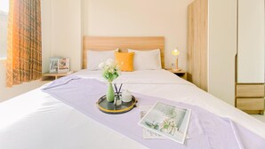 Un lit bien fait, recouvert d’une couvre-lit violette, une table de chevet avec une lampe et une armoire.