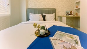 Een netjes opgemaakt bed met witte beddengoed en een blauw accent, een dienblad met decoratieve items, en een krant op het bed.