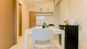 Een compacte keuken met witte kasten, een zwarte koelkast en een kleine eettafel met een witte stoel.
