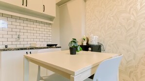 Een moderne keuken met witte kastjes, een betegelde achterwand, een witte tafel en een potplant.