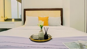 A hotel room with a neatly made bed, a bedside table with a lamp, and a tray with toiletries. - Good Place and Comfy 2BR at Podomoro Golf View Apartment (Gunung Putri)