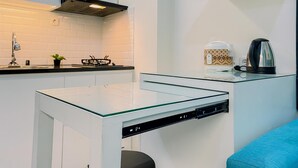A modern kitchen with white cabinetry, a glass-top table, a built-in stove, and a coffee maker on a shelf. - Good Place and Comfy 2BR at Podomoro Golf View Apartment (Gunung Putri)