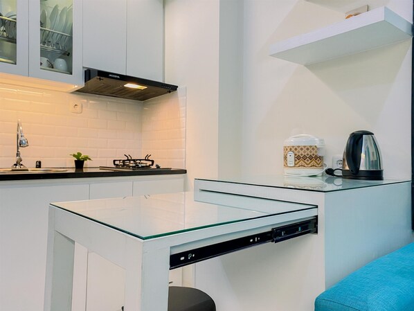 A modern kitchen with white cabinetry, a glass-top table, a built-in stove, and a coffee maker on a shelf.