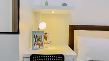 A neatly arranged hotel room with a bedside table, a chair, a bed with white bedding, a book titled "Scandinavian Dreaming," and a small green bottle on the nightstand.