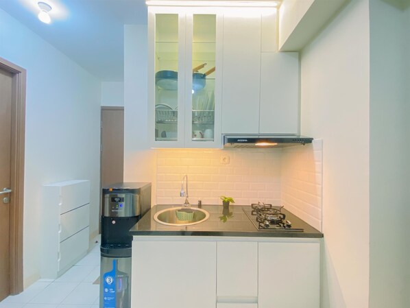 A compact kitchen with white cabinets, a stainless steel range hood, a built-in sink, and a coffee maker. - Good Place and Comfy 2BR at Podomoro Golf View Apartment (Gunung Putri)