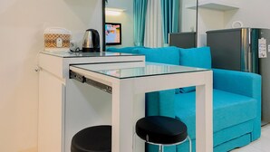 A compact living space with a kitchenette, a sofa, a coffee maker, a kettle, a TV, and a refrigerator. - Good Place and Comfy 2BR at Podomoro Golf View Apartment (Gunung Putri)