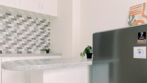 A modern kitchen with white cabinets, a granite countertop, and a stainless steel refrigerator. - Modern 2BR Apartment at Podomoro Golf View (Gunung Putri)