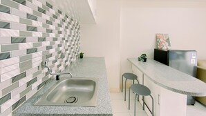 A modern kitchen with a stainless steel sink, a tiled backsplash, and a granite countertop. There are two stools and a small potted plant on the counter. - Modern 2BR Apartment at Podomoro Golf View (Gunung Putri)
