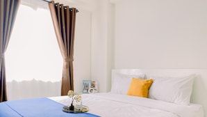 A neatly made bed with white and yellow pillows, a blue bedspread, and a decorative item on the bed. - Modern 2BR Apartment at Podomoro Golf View (Gunung Putri)
