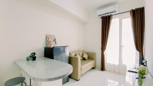 A modern living room with a kitchen area, a beige sofa, a small table with a plant, and a painting on the wall. - Modern 2BR Apartment at Podomoro Golf View (Gunung Putri)