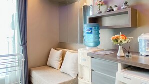 Habitación de hotel con sofá, dispensador de agua, refrigerador Samsung y una estantería con objetos decorativos.