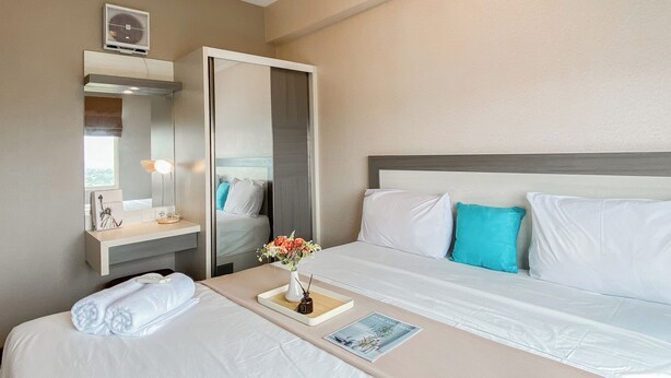 Una habitación de hotel con cama, una mesita de noche con lámpara, un espejo y un pequeño jarrón con flores.