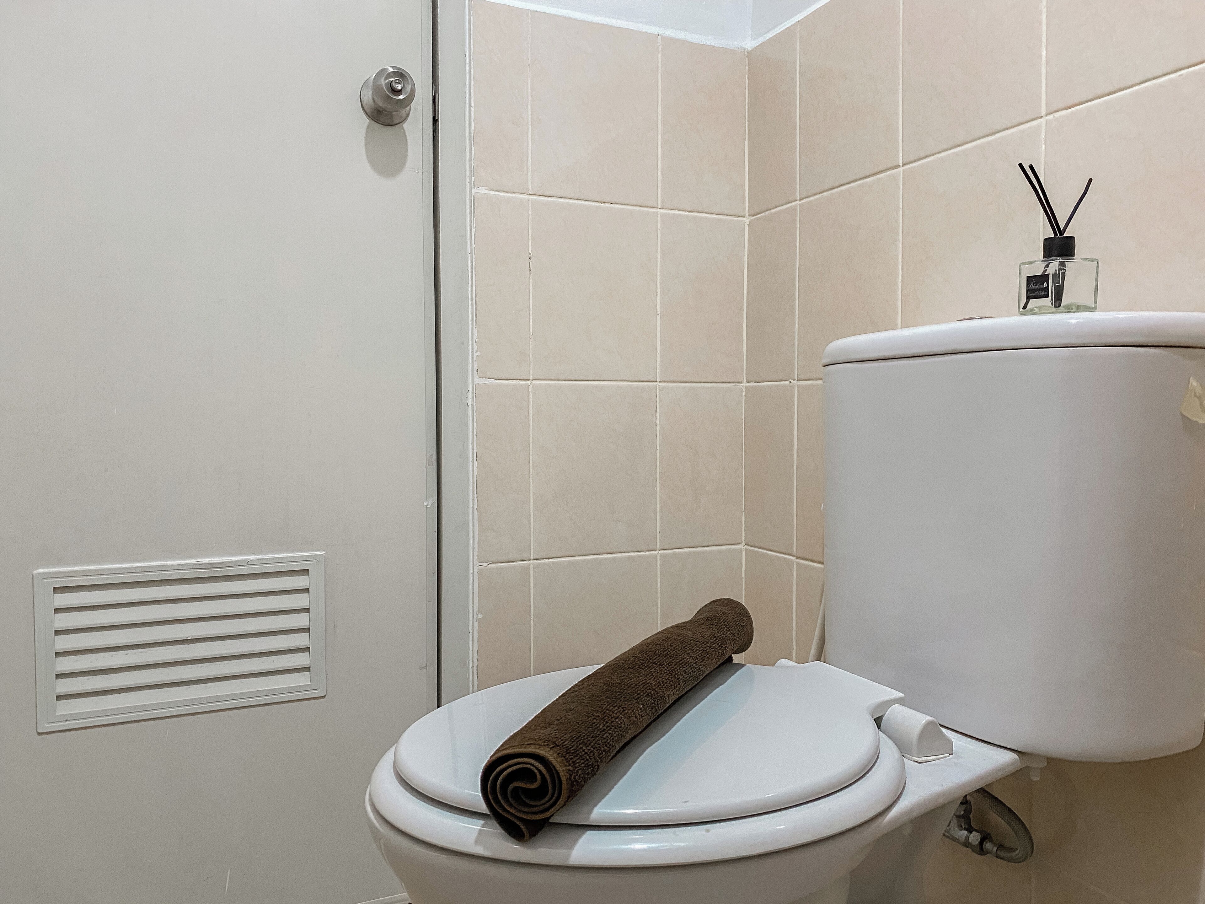 Een badkamer met een toilet, een handdoek op de deksel, en een toiletrolhouder met een fles handzeep.