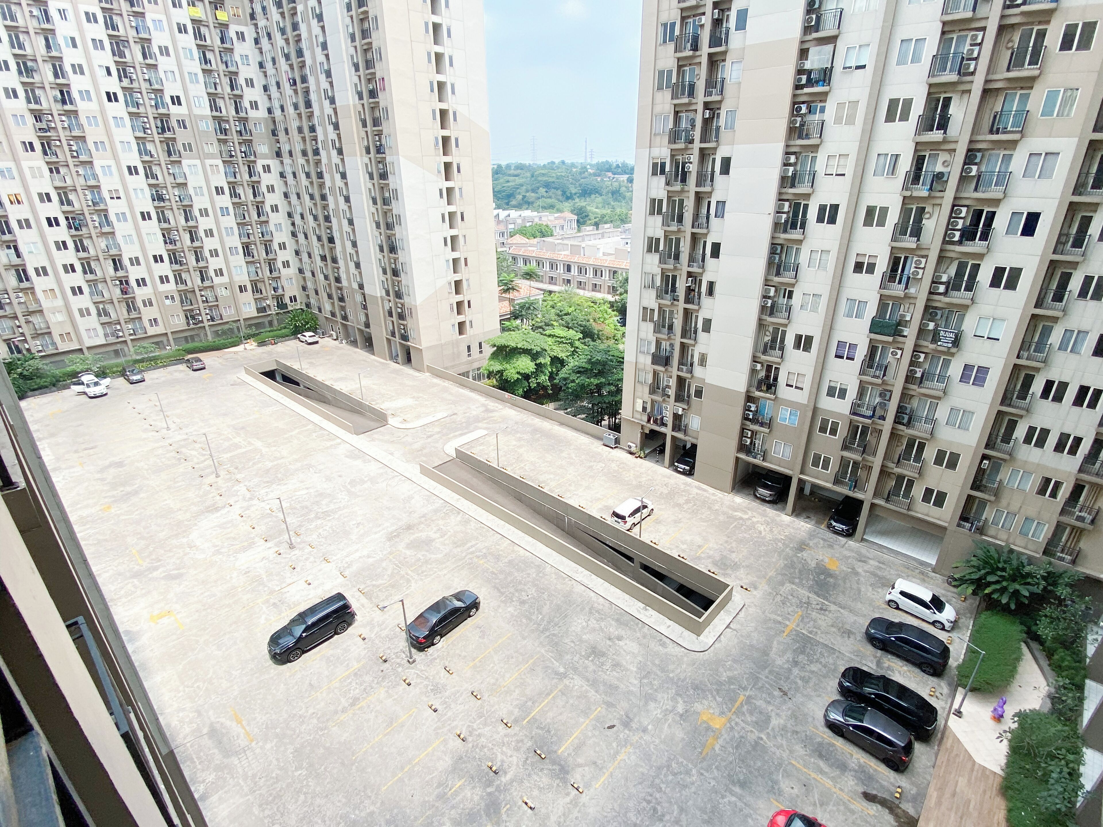 A high-rise residential building with multiple balconies and a parking area.