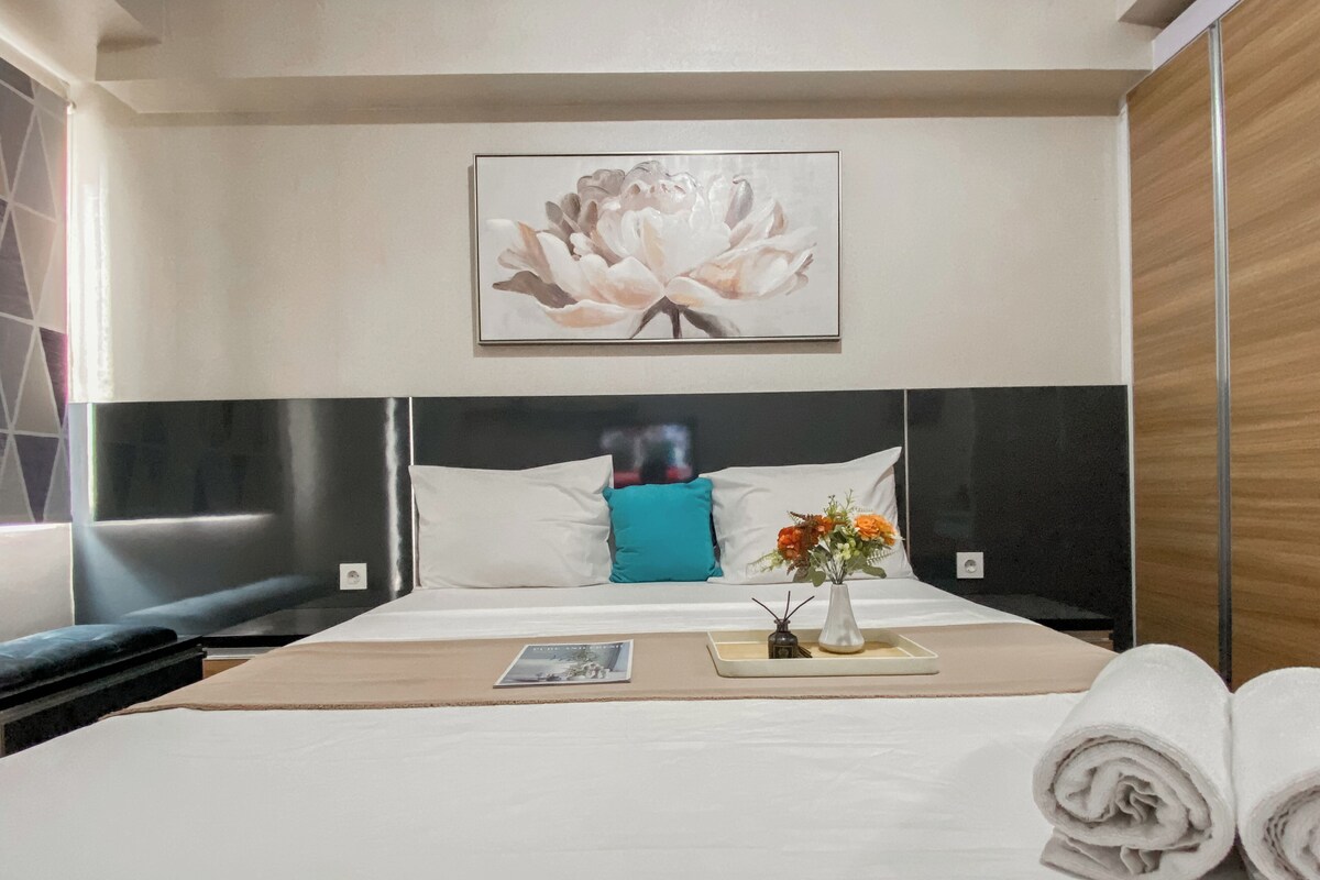 A hotel room with a bed, a nightstand, a vase with flowers, and a framed picture on the wall.