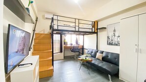 A compact room with a bunk bed, a desk, a chair, a sofa, a television, and a poster of New York City. - Tranquil and Homey Studio at Podomoro Golf View Apartment (Gunung Putri)