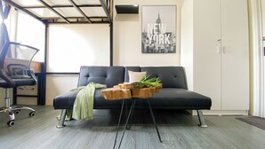 A modern office space with a black sofa, a wooden side table, and a chair. A framed picture of New York City is on the wall. - Tranquil and Homey Studio at Podomoro Golf View Apartment (Gunung Putri)