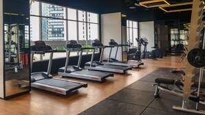 Un gimnasio con cintas de correr, máquinas de pesas y grandes ventanales con vistas a edificios.