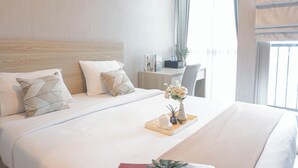 Una habitación de hotel con una cama bien hecha, un escritorio pequeño y una ventana con cortinas.