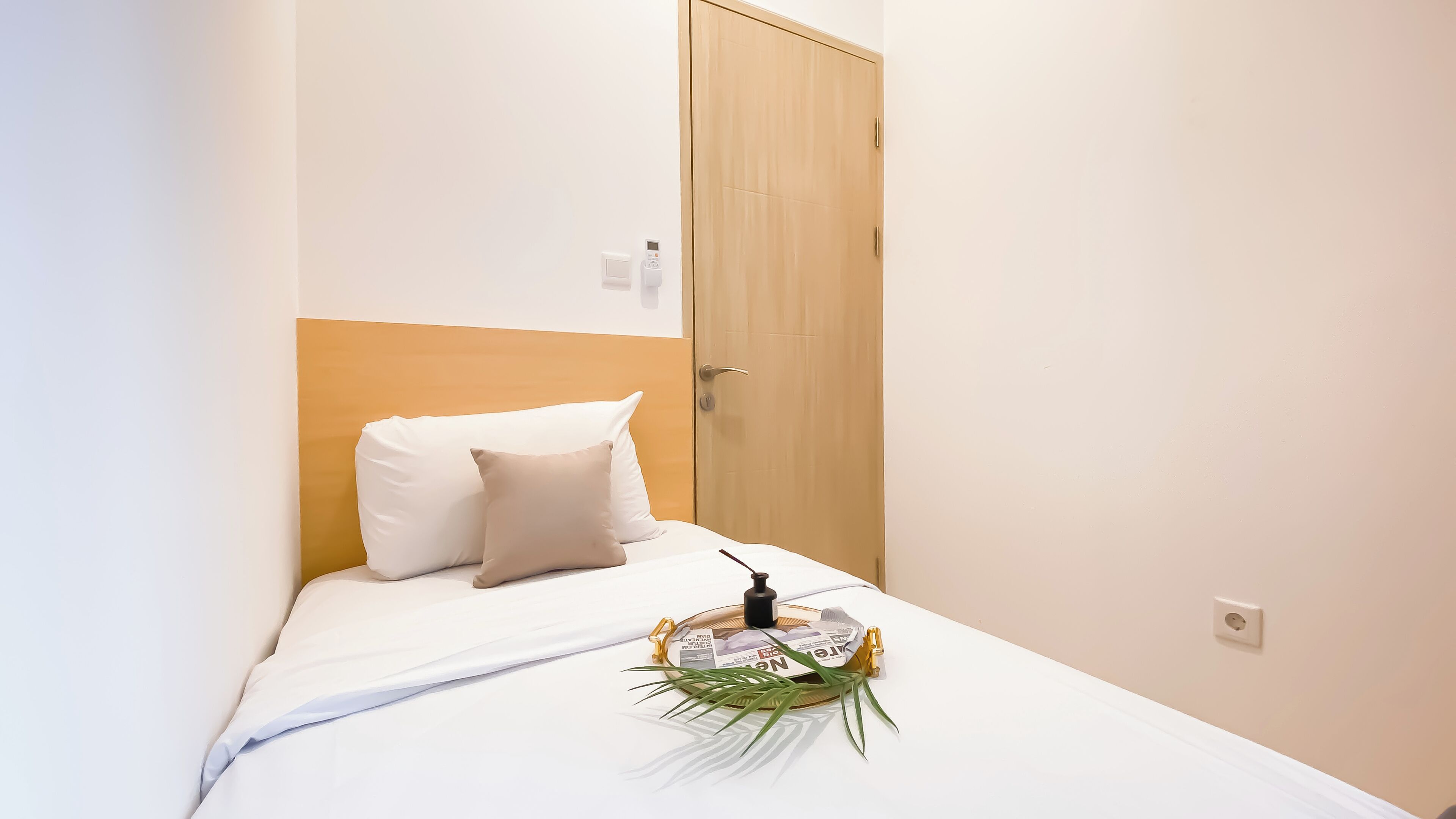 A neatly made bed with white bedding and two pillows, a small bedside table with a bottle and a tissue box, and a wooden wardrobe.