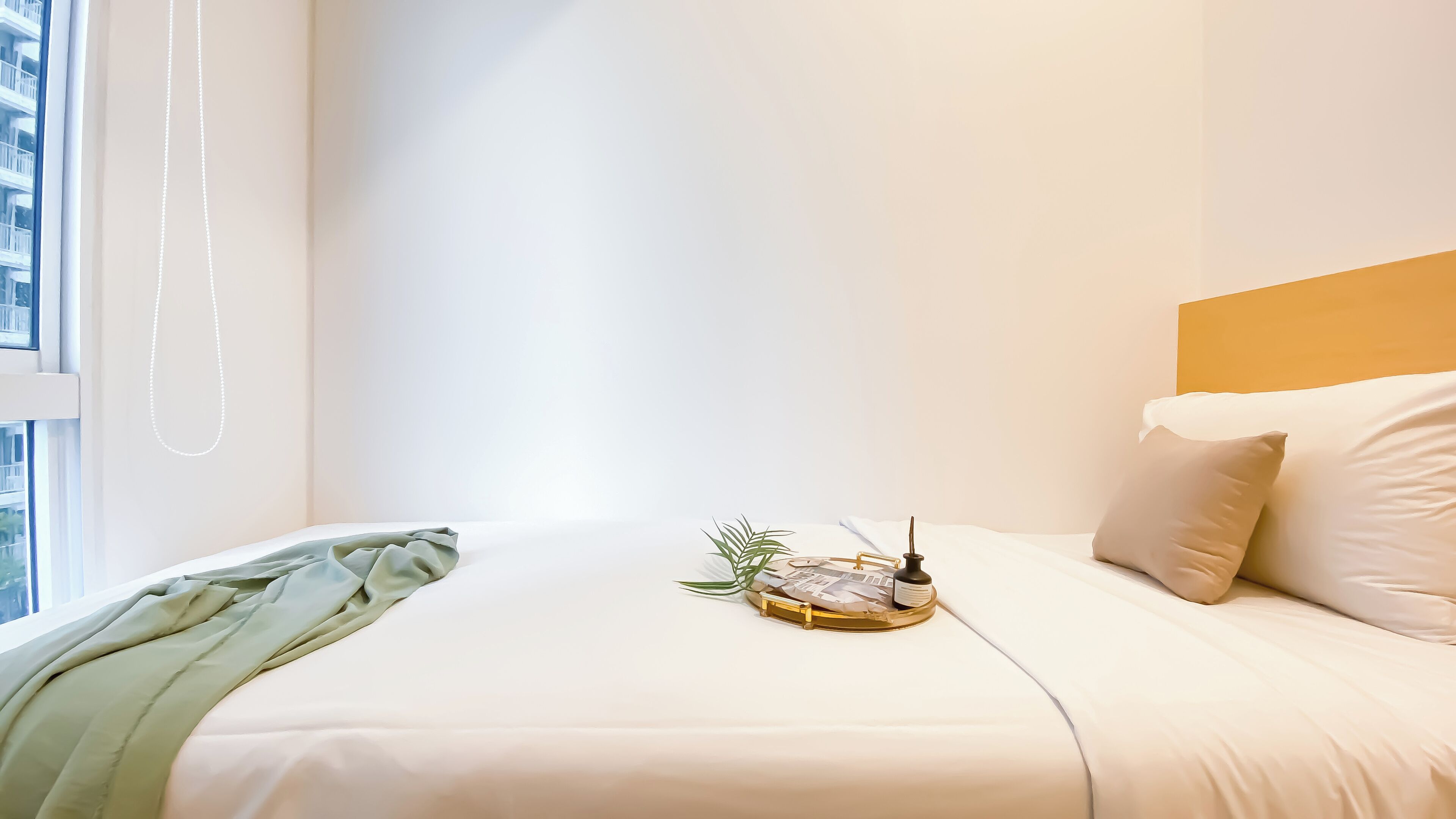 A neatly made bed with white bedding, a green throw blanket, and a small tray with a plant and a bottle.