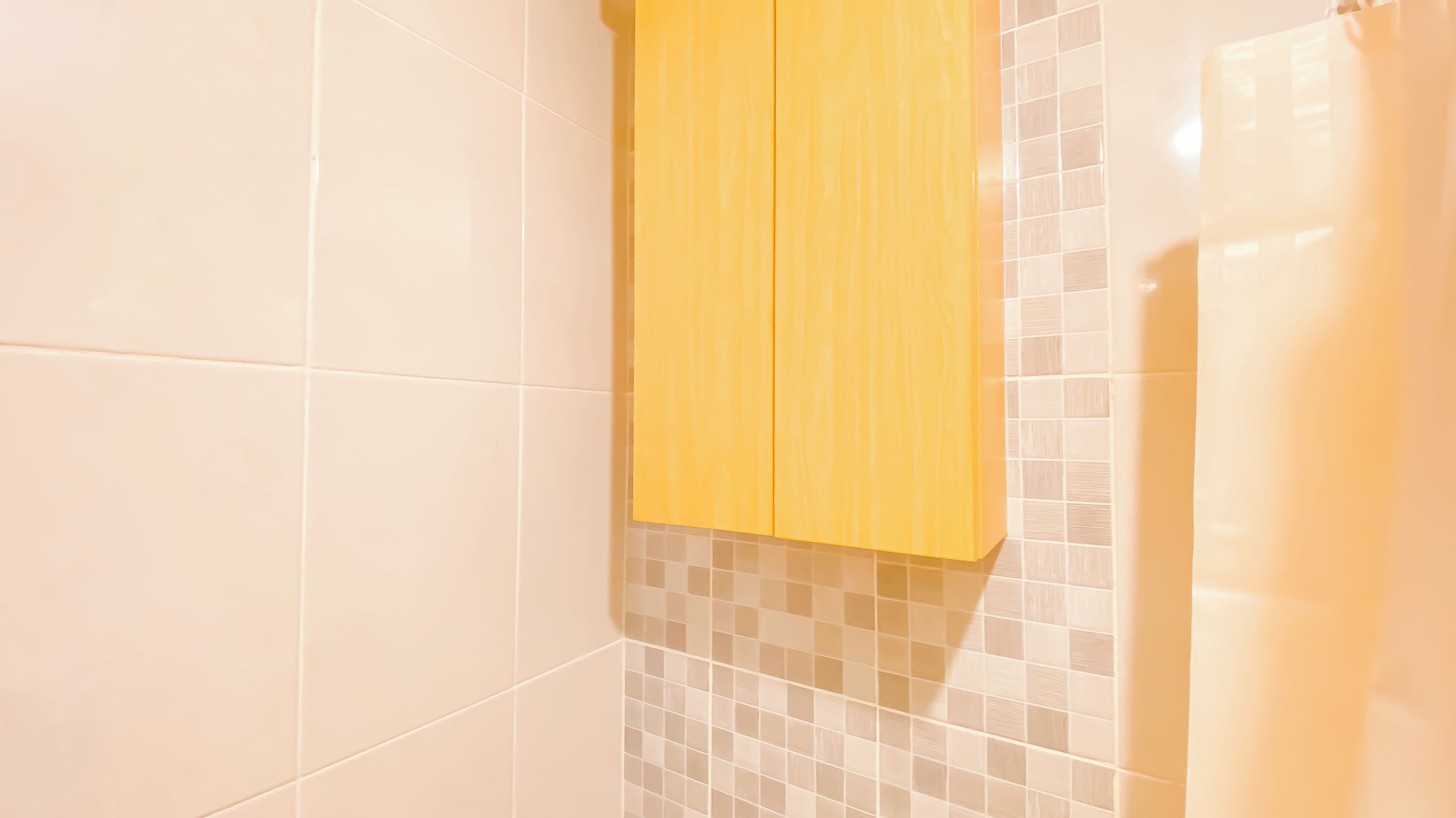 A bathroom with white tiles, a yellow cabinet, and a shower curtain.