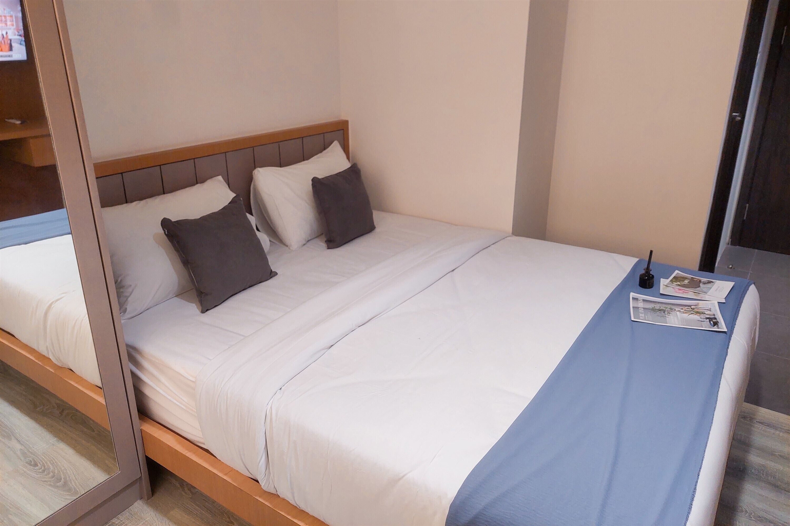 A neatly made bed with white and gray bedding, a wooden headboard, and a blue accent at the foot of the bed.