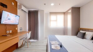 Ein Hotelzimmer mit einem Bett, einem Schreibtisch mit Stuhl, einem Fernseher und einem Fenster mit Vorhängen.