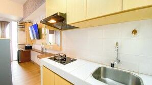 A modern kitchen with white tiles, a stainless steel sink, a gas stove, wooden cabinets, and a built-in oven. - Minimalist and Homey Studio at Tokyo Riverside PIK 2 Apartment (Teluknaga)