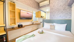 A hotel room with a bed, a TV mounted on the wall, a minibar, and a bathroom mirror. - Minimalist and Homey Studio at Tokyo Riverside PIK 2 Apartment (Teluknaga)