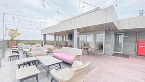 An outdoor seating area with wicker furniture, a pink sofa, and string lights. - Good Homey Studio Apartment at Warhol (W/R) Residences (Semarang)