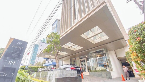 A modern building with a prominent entrance, a sign for 'LOUIS KIMNE', and a car parked in front. - Good Homey Studio Apartment at Warhol (W/R) Residences (Semarang)