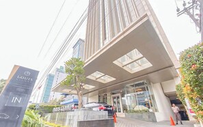 A modern building with a prominent entrance, a sign for 'LOUIS KIMNE', and a car parked in front. - Good Homey Studio Apartment at Warhol (W/R) Residences (Semarang)