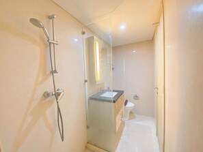A modern bathroom with a glass shower enclosure, a sink, and a toilet. - Good Homey Studio Apartment at Warhol (W/R) Residences (Semarang)