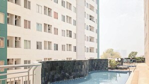 A modern apartment building with a rooftop pool area featuring a stone wall and a clear blue pool. - Best Choice and Restful Studio at Pavilion Permata Apartment (Surabaya)