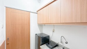 A small kitchen with wooden cabinets, a black countertop, a sink, and a black induction cooktop. - Best Choice and Restful Studio at Pavilion Permata Apartment (Surabaya)