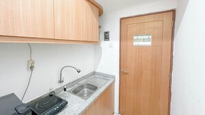 A small kitchen with wooden cabinets, a granite countertop, a built-in sink, and a stove. - Best Choice and Restful Studio at Pavilion Permata Apartment (Surabaya)