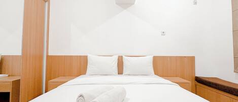 A hotel room with a large bed, wooden headboard, white bedding, and a neatly folded towel on the bed.