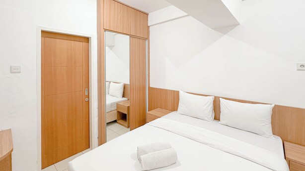A modern bedroom with a wooden wardrobe, a bed with white bedding, and a mirror. - Best Choice and Restful Studio at Pavilion Permata Apartment (Surabaya)