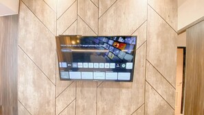 A flat-screen TV mounted on a wall with a geometric pattern. - Cozy and Homey Studio at The Alton Apartment (Semarang)