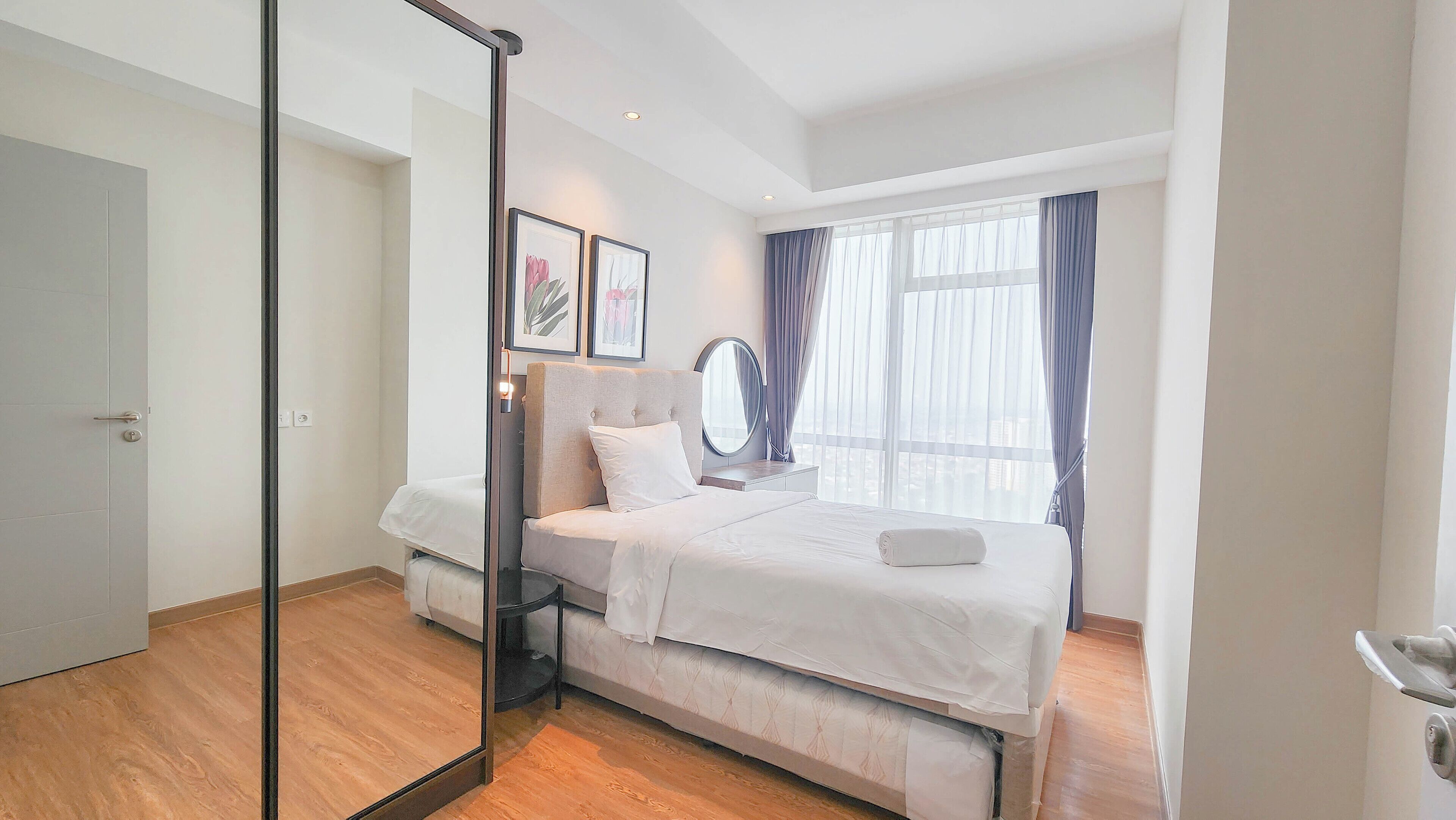 Ein modernes Hotelzimmer mit einem großen Bett, einem Spiegel am Nachttisch und einem Fenster mit Vorhängen.