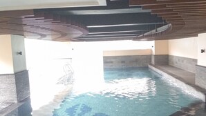An indoor swimming pool with clear water, tiled floor, and a modern architectural design with a sloped ceiling and stone walls.