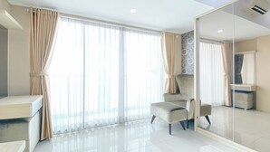 A modern hotel room with a large mirror, a plush armchair, and a large window with sheer curtains.